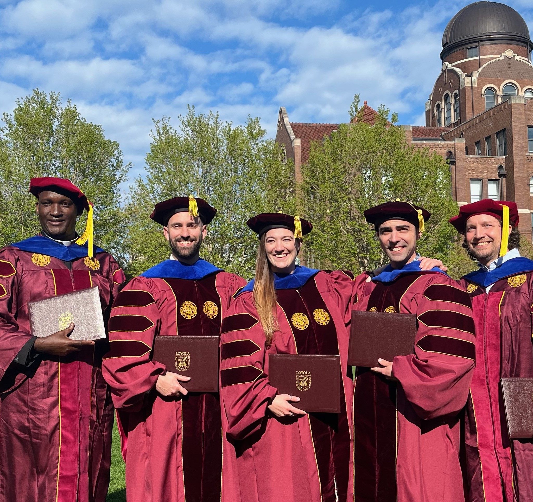 Graduate students holding diplomas outside Graduate students holding diplomas outside